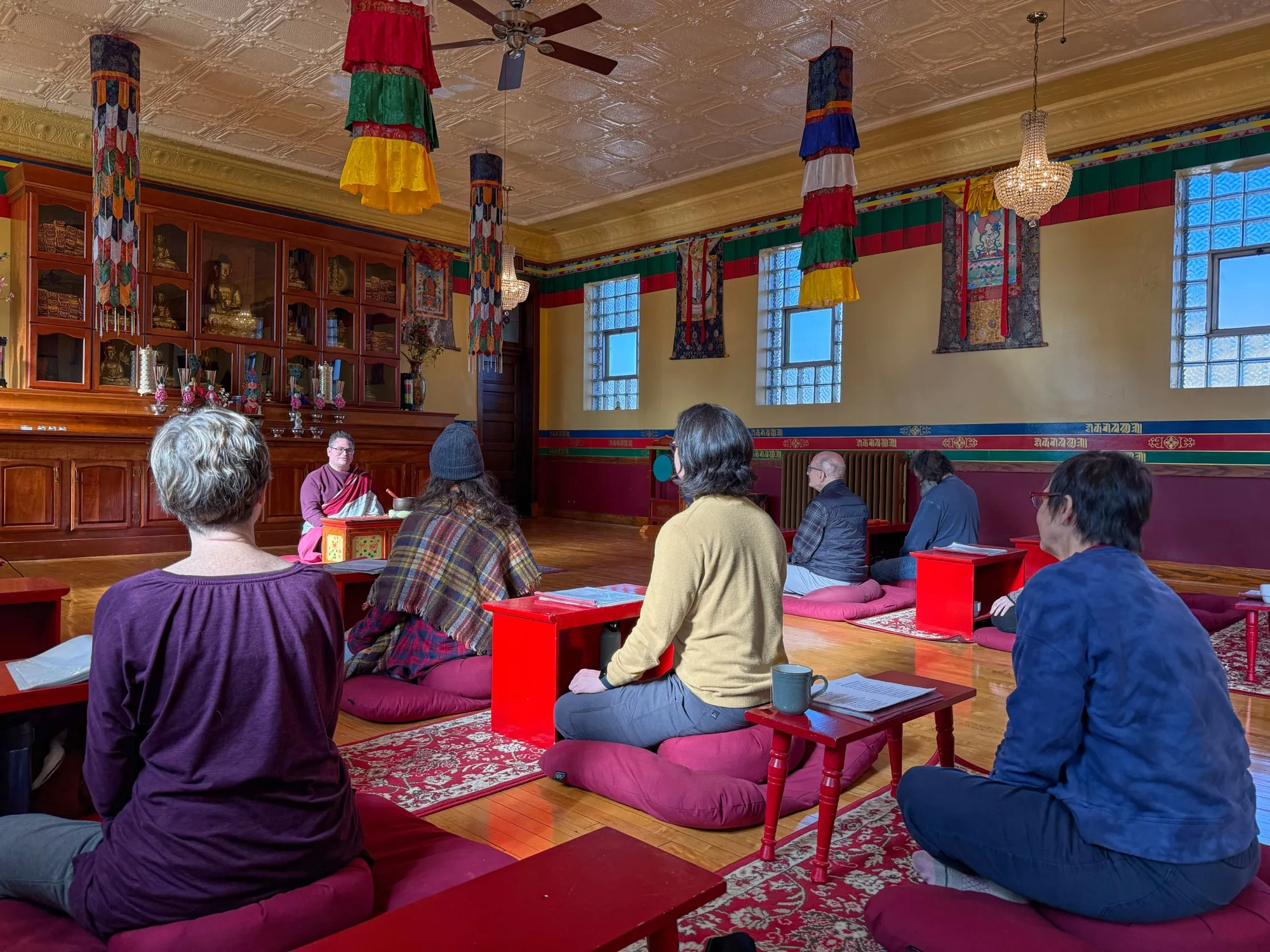 Practitioners seated on cushions at low red benches during a Sunday session in the Chicago KTC shrine room, with the teacher at the front