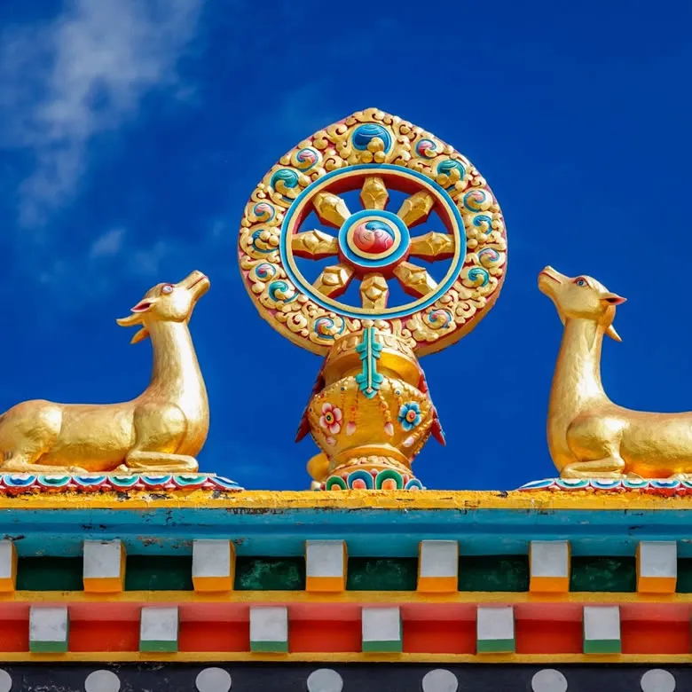 Golden dharma wheel flanked by two deer on a monastery roof against a deep blue sky