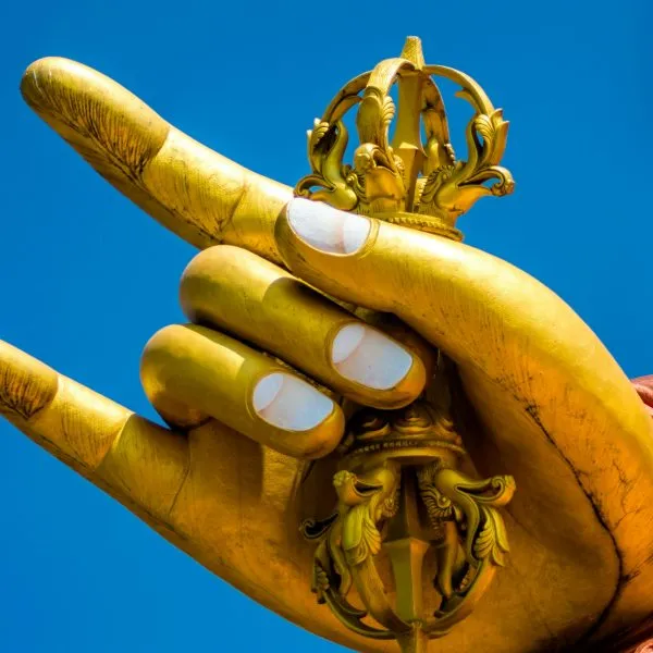 Golden statue hand holding a vajra against a blue sky