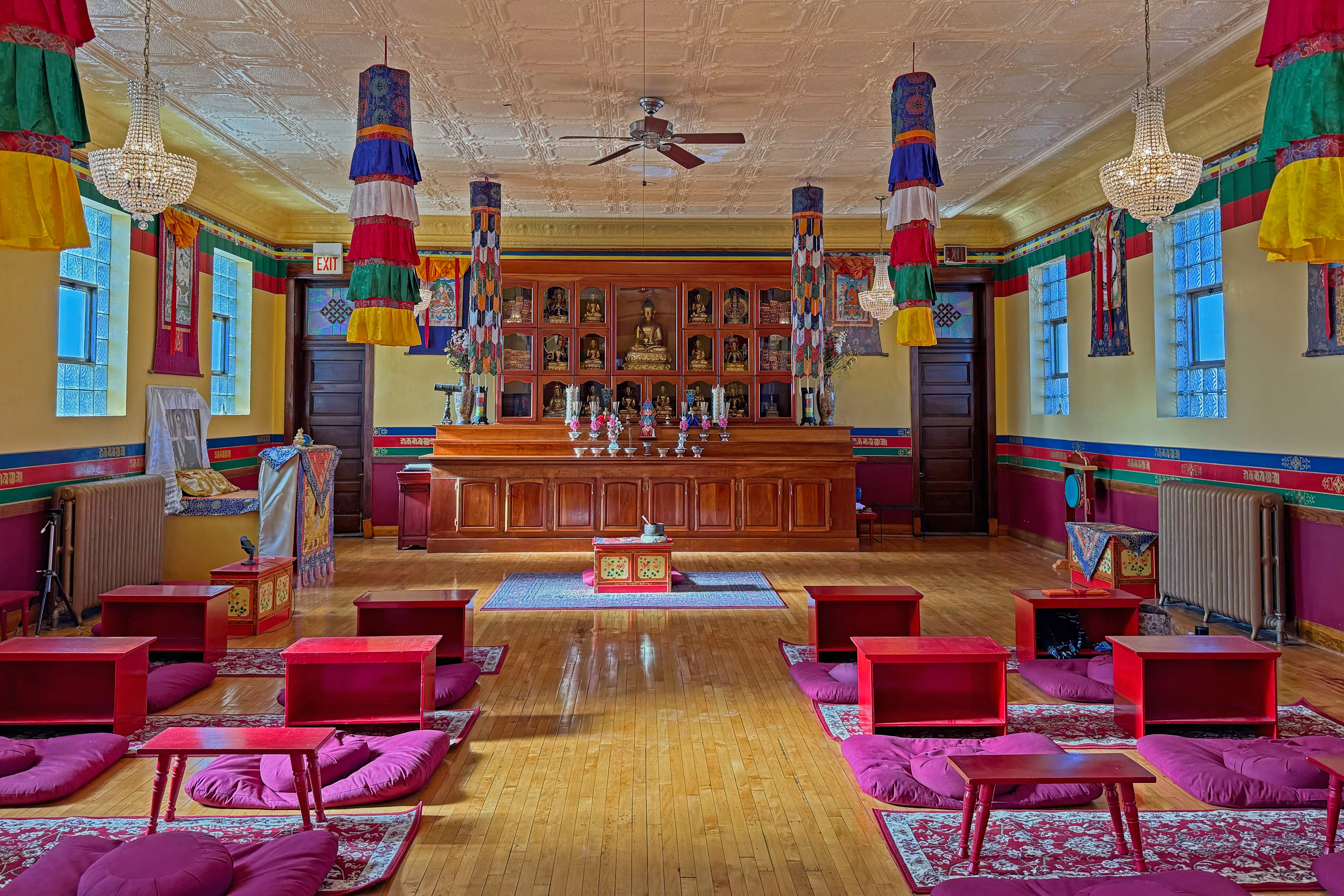 The Chicago KTC shrine room — rows of meditation cushions and low red tables facing the gilded altar, with hanging Tibetan banners and crystal chandeliers overhead